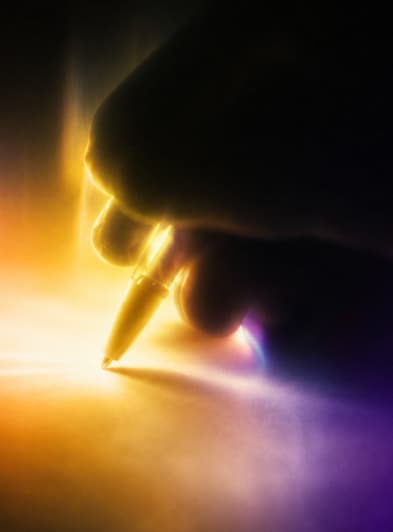 Close-up of a hand signing a partnership agreement with a pen under coloured light, representing brand and creator client partnerships